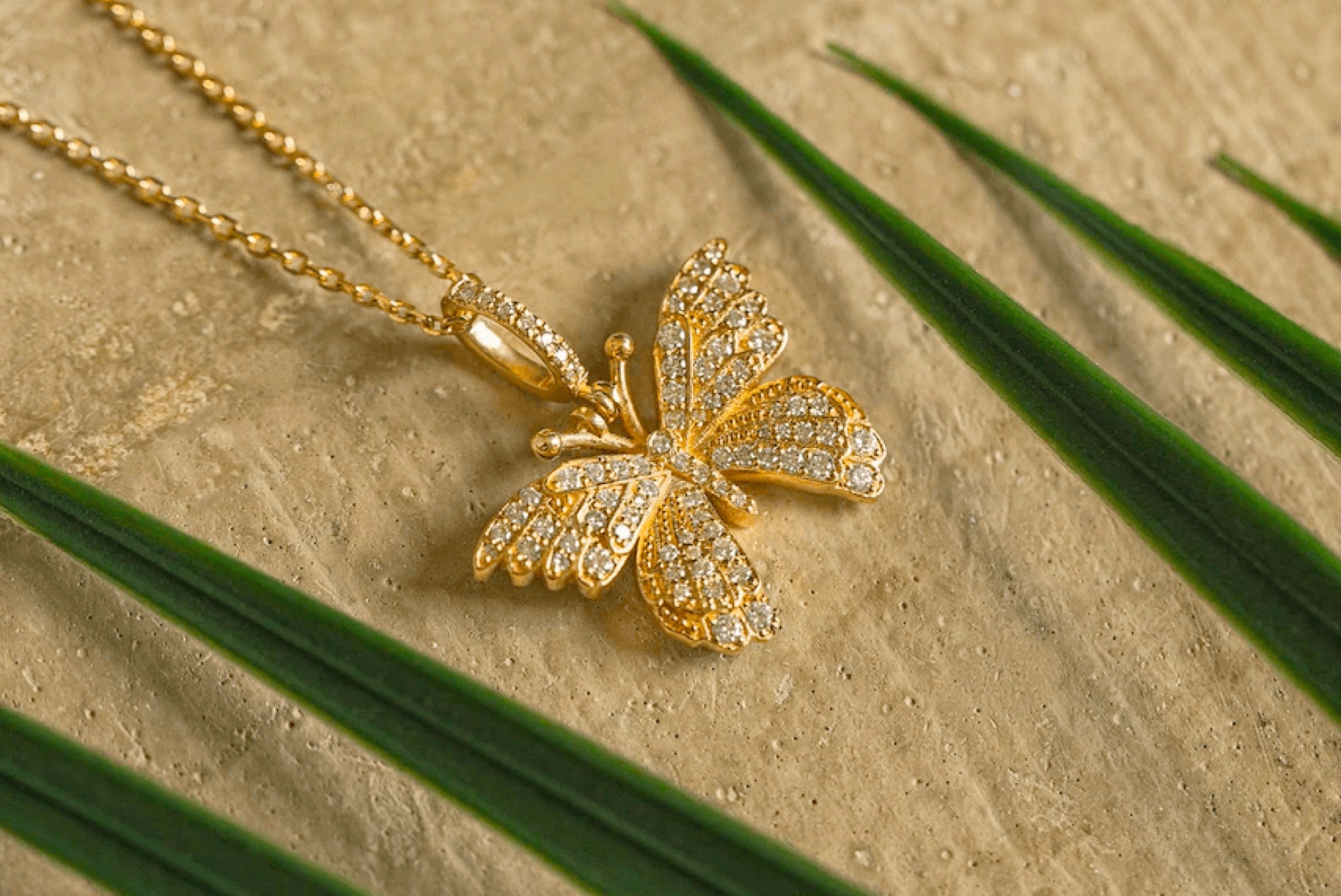 Gold butterfly necklace on stone framed by green leaves